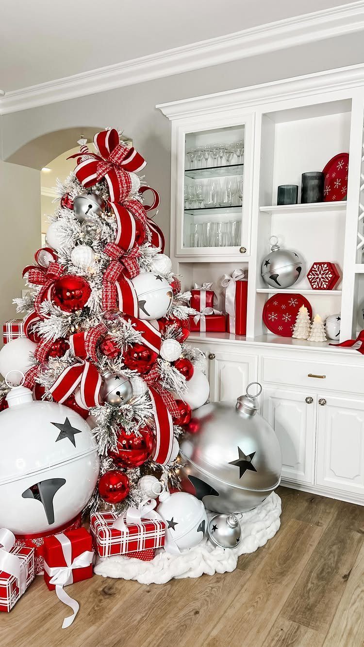 White flocked Christmas tree decorated with red striped ribbons and large ornaments.