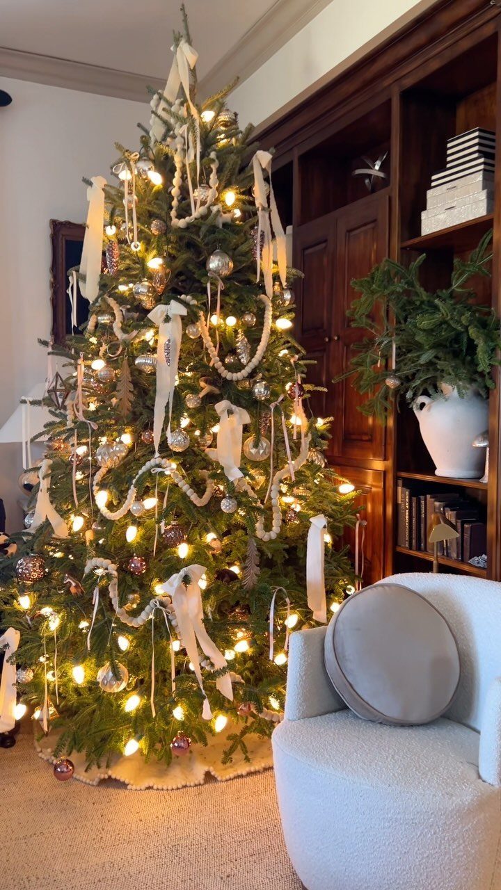 Christmas tree decorated with warm lights, ornaments, and short white ribbon strips.