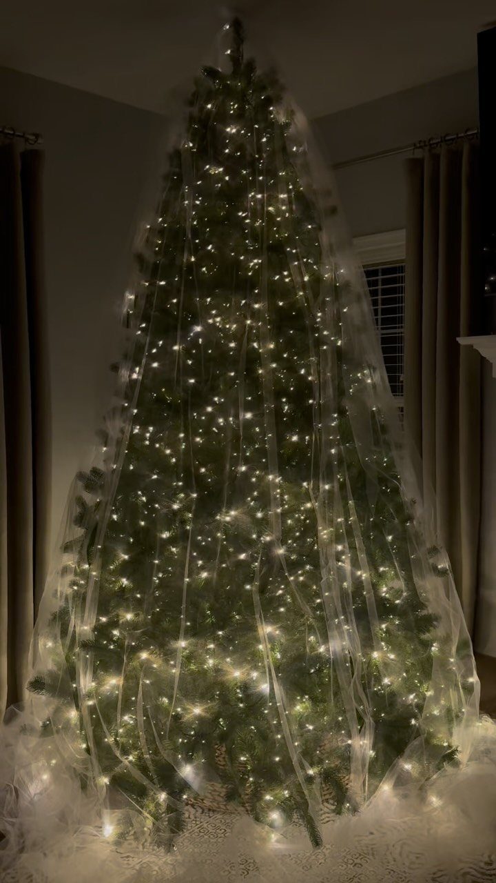 Christmas tree decorated with white lights and sheer white tulle ribbon draping vertically.