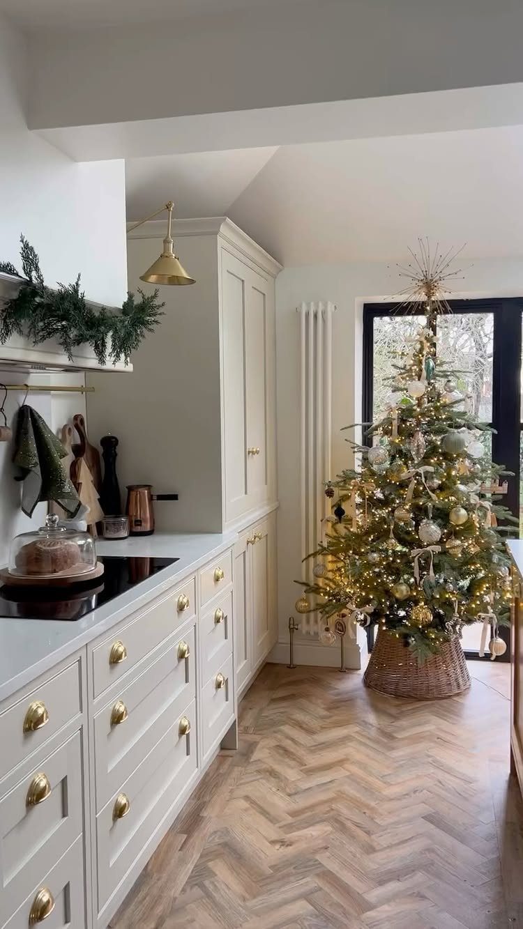 Decorated Christmas tree standing on a herringbone wood floor in a white kitchen