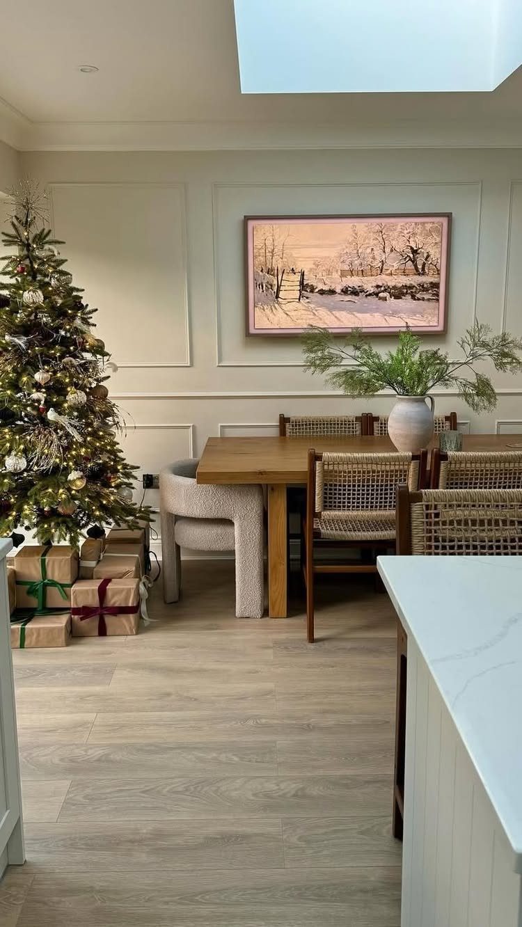 Decorated Christmas tree with presents next to a wooden dining table in a kitchen