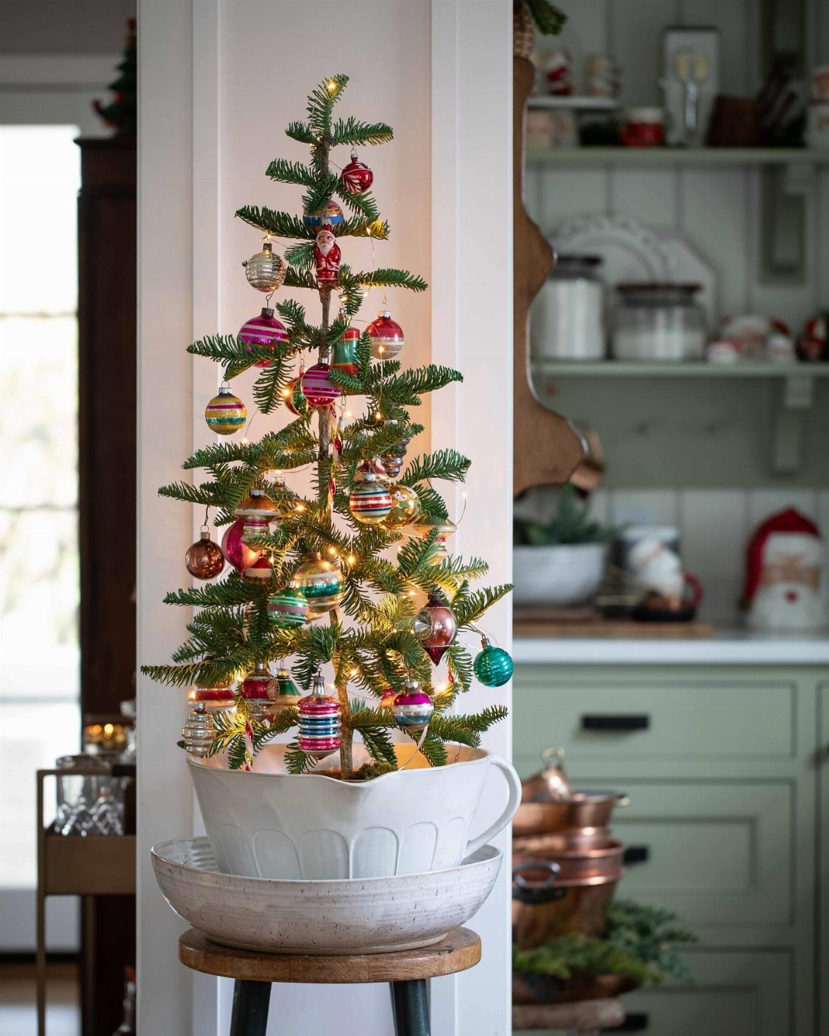 Small decorated Christmas tree in a white pot placed in a kitchen setting.
