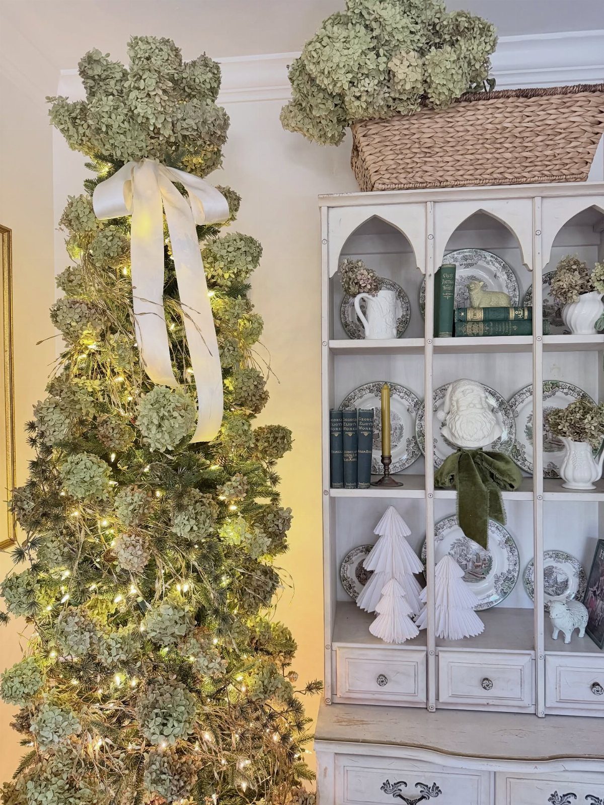 Hydrangea decorated Christmas tree with white ribbon next to a white vintage hutch