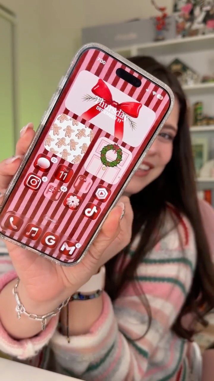 Smartphone with a cute Christmas wallpaper featuring red stripes and holiday icons.