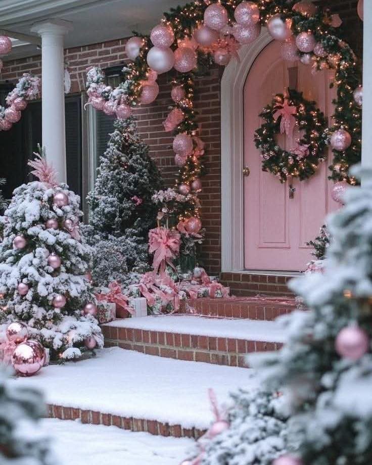 Pink front door decorated with a pink wreath and snowy Christmas trees