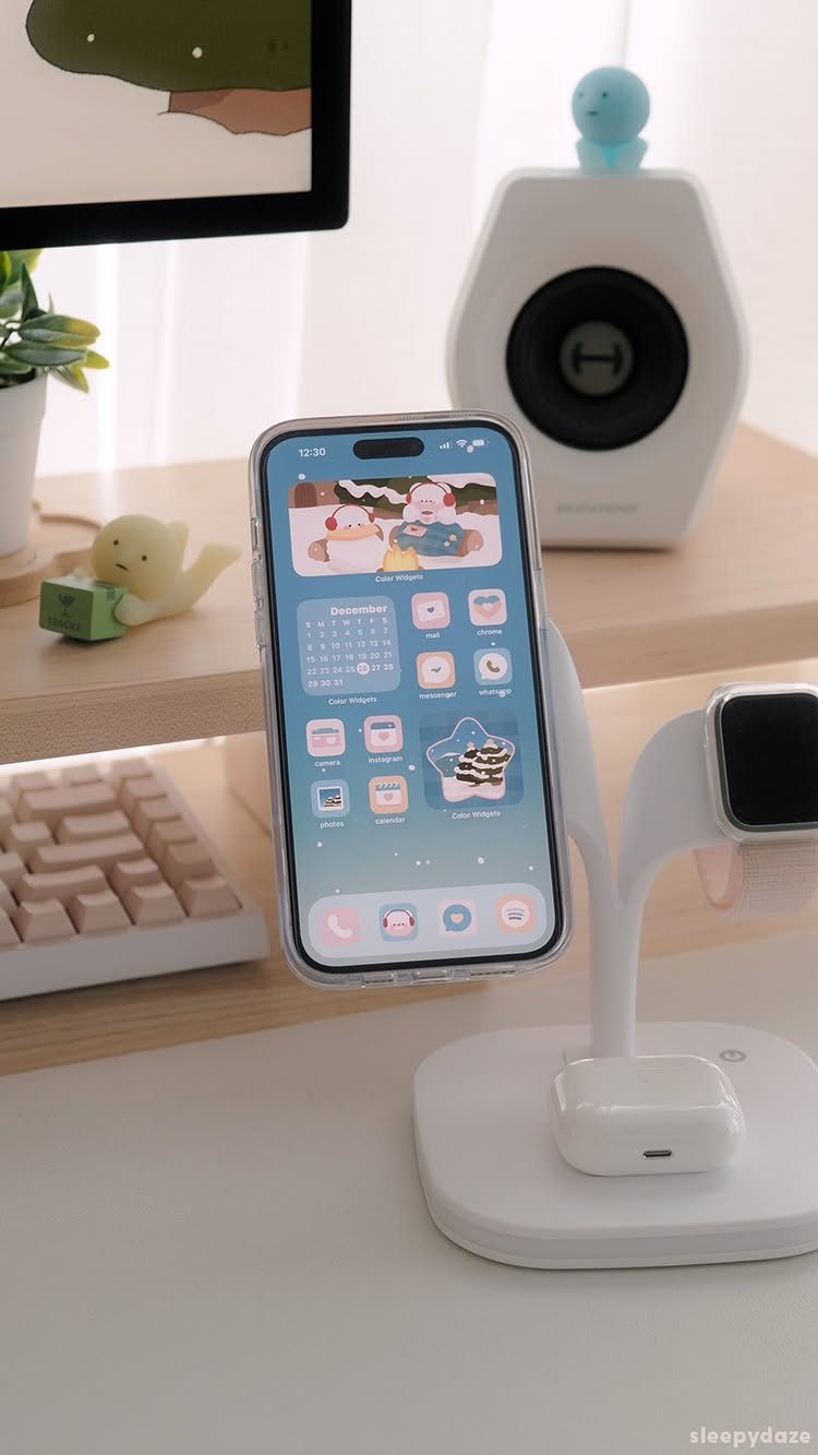 iPhone on a desk showing a cute snowy Christmas wallpaper with characters.