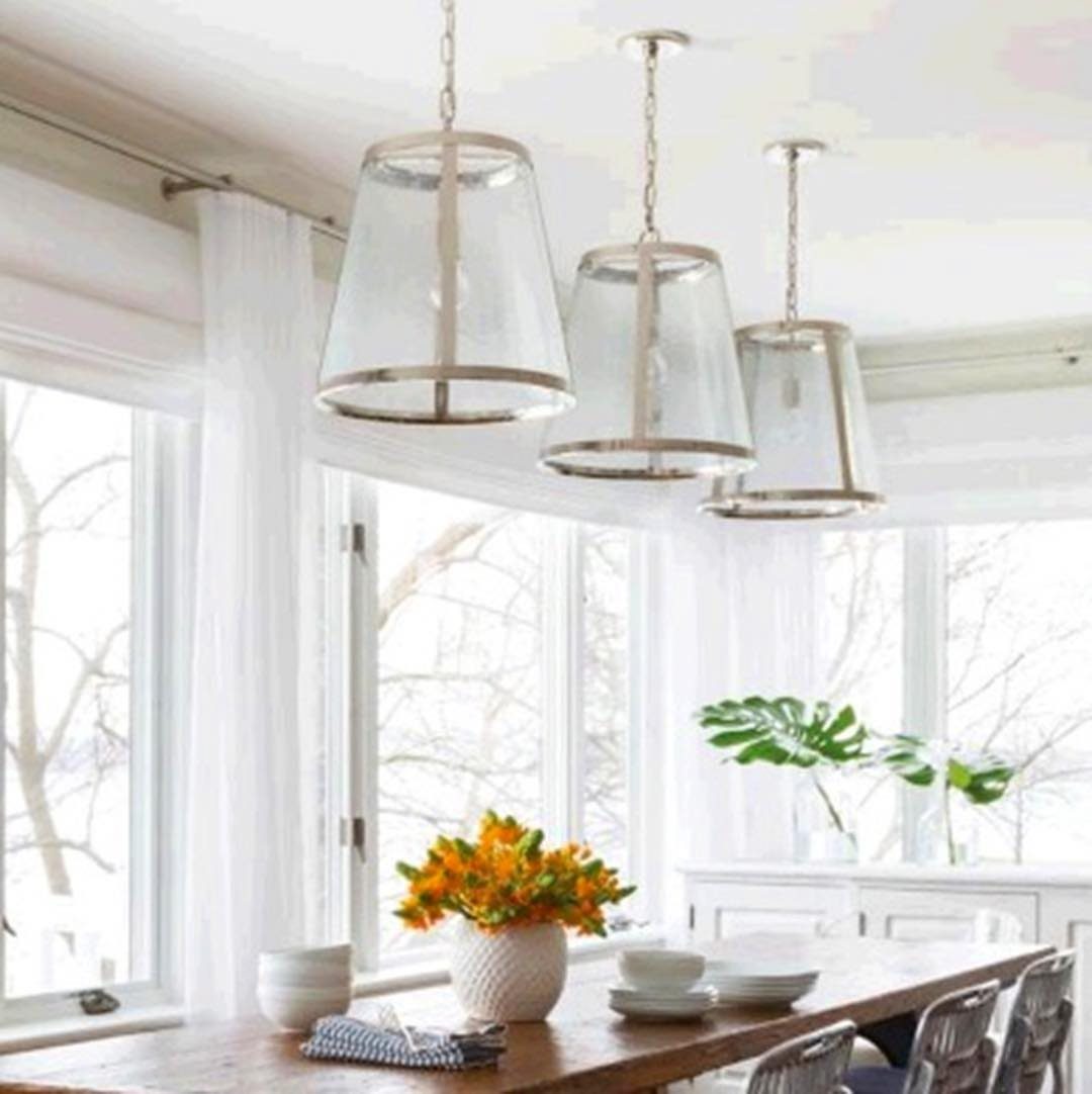 Three glass pendant lights hanging over a wooden dining table in a bright room.