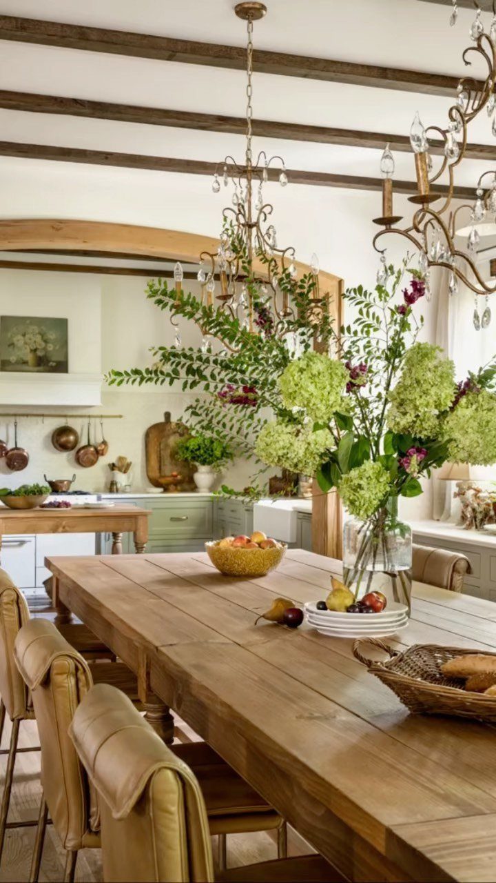 Wooden dining table with leather chairs under an ornate crystal chandelier and beams.