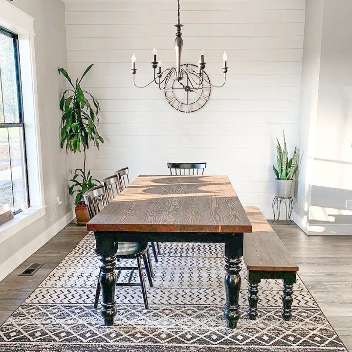 Wooden dining table and bench against white shiplap walls with a black chandelier.