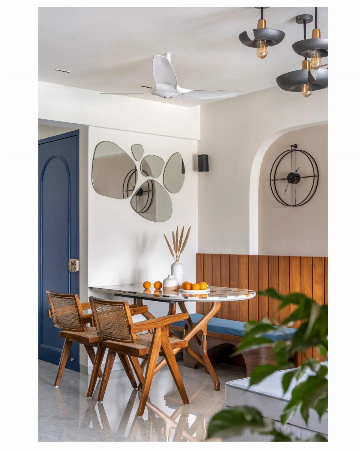 Dining area with marble table, blue banquette, and organic shaped wall mirrors.