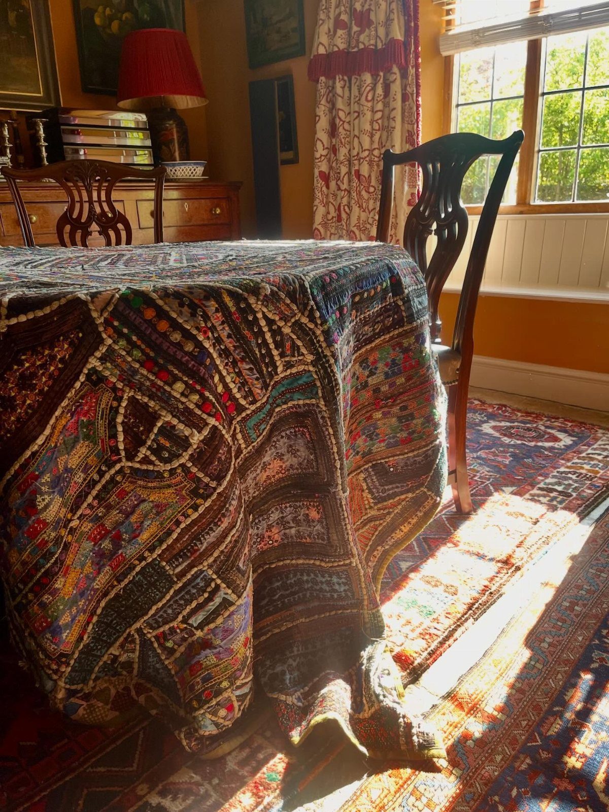 Small dining table with colorful woven cloth and wooden chairs in a corner room
