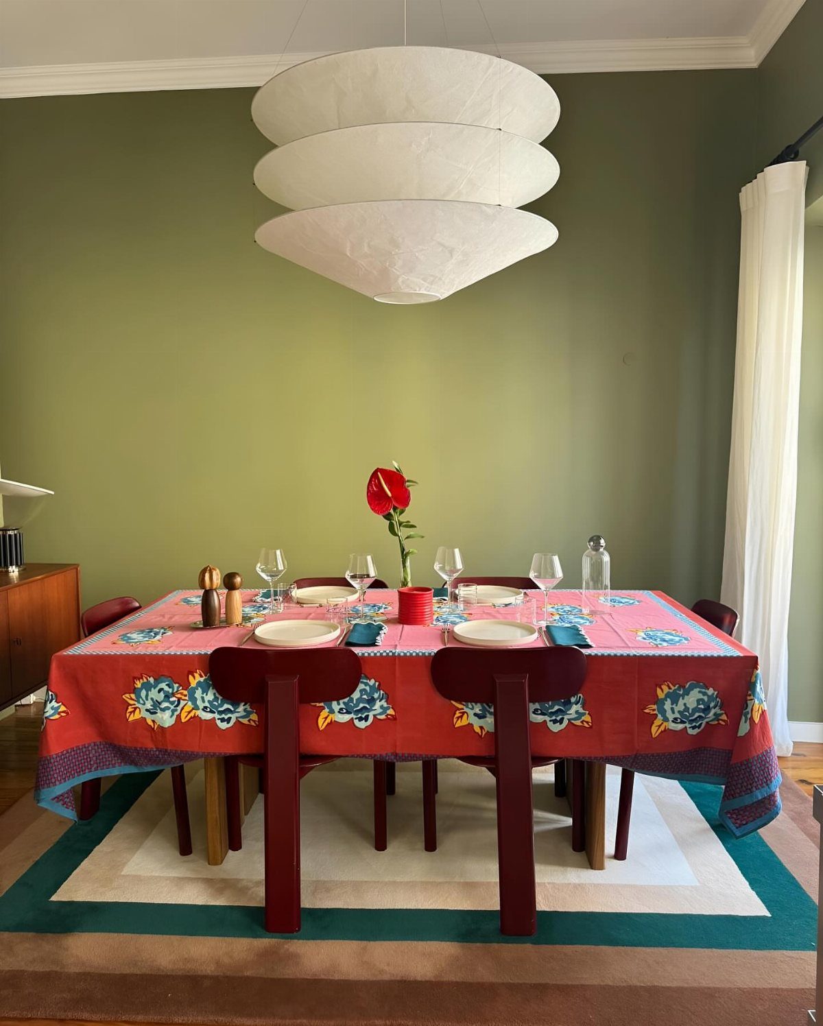 Dining table with red floral cloth on a cream and green rug.