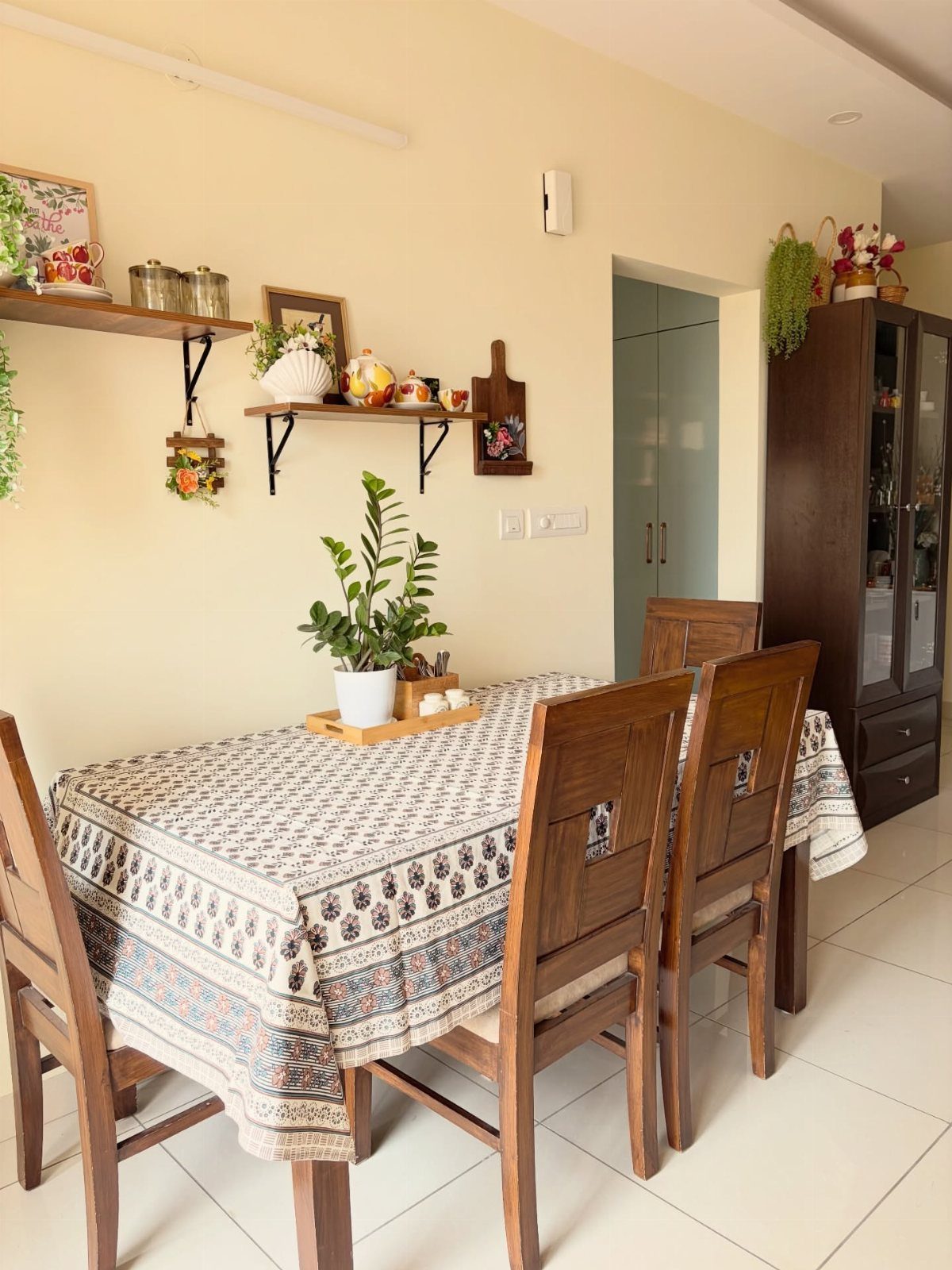 Wooden dining table with patterned cloth and chairs against a cream wall.