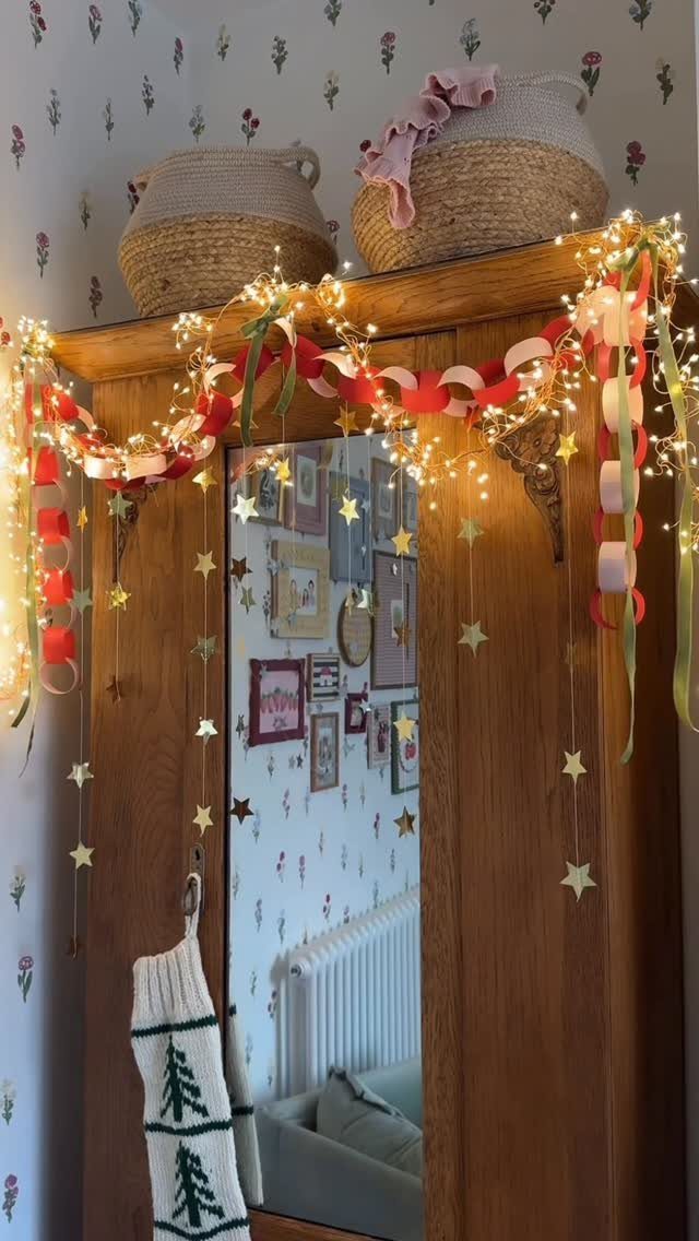 Wooden wardrobe decorated with warm fairy lights, red garlands, and hanging gold stars.