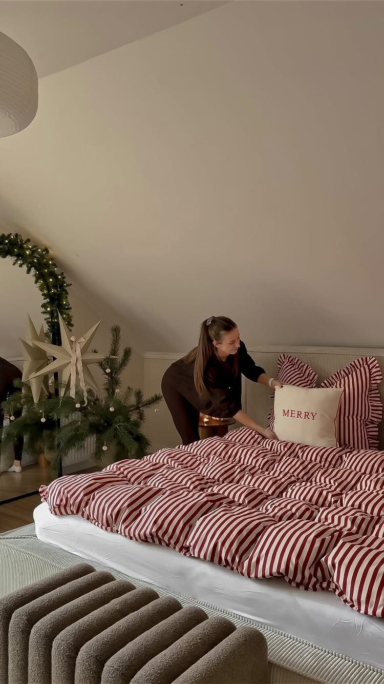 Woman arranging red and white striped bedding in a cozy Christmas themed bedroom