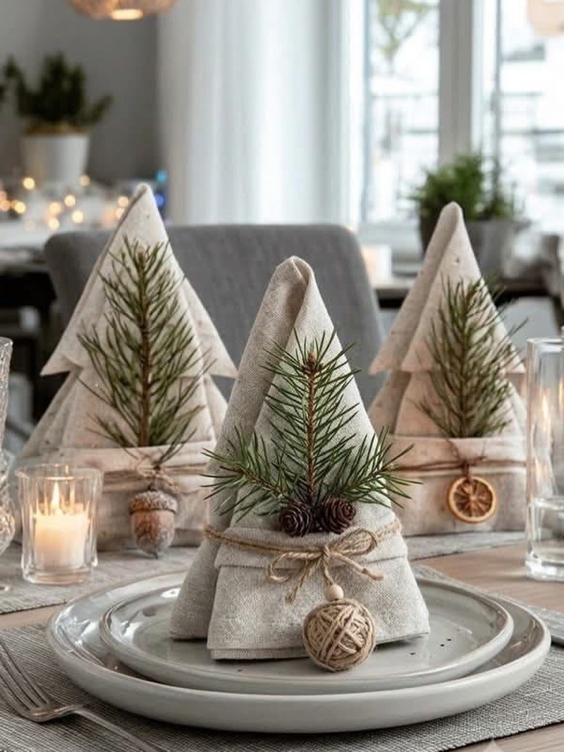 Napkins folded as trees with fresh pine sprigs and pinecones on white plates.
