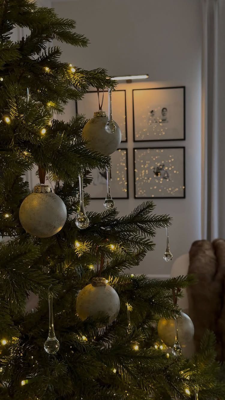 Decorated Christmas tree with warm lights and pale ornaments against a white wall