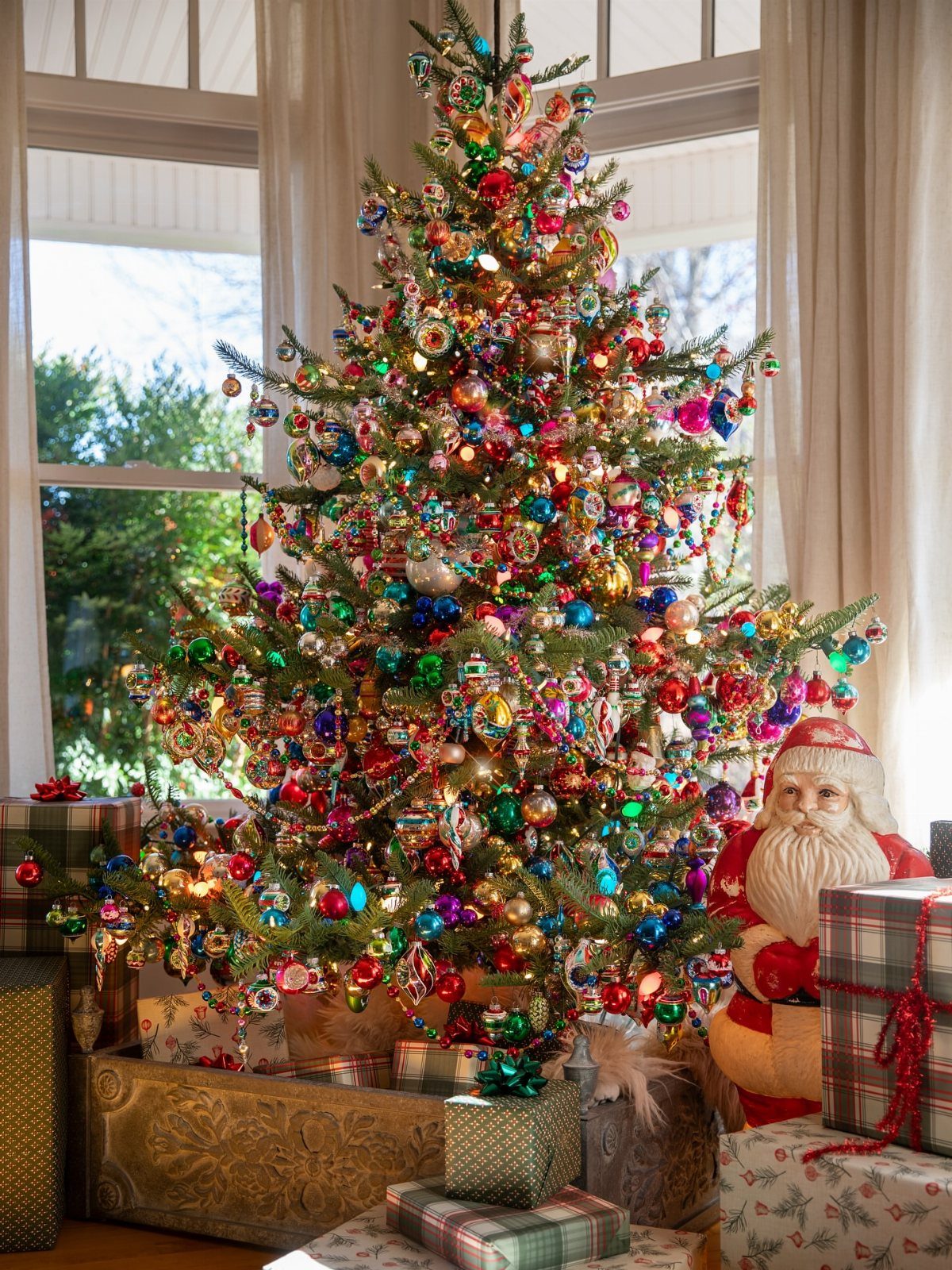 Christmas tree decorated with colorful vintage ornaments and tinsel next to a Santa figure.