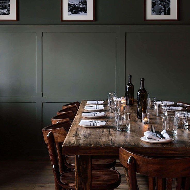 Rustic wooden dining table set for a meal against dark green paneled walls.