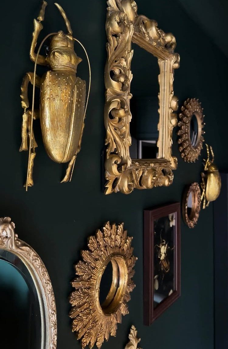 Ornate gold frames and a golden beetle sculpture on a dark green wall.