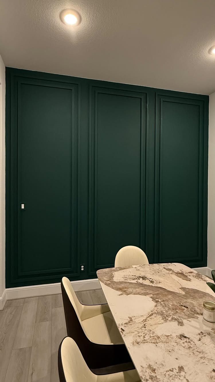 Dark green paneled wall behind a marble dining table with cream chairs.