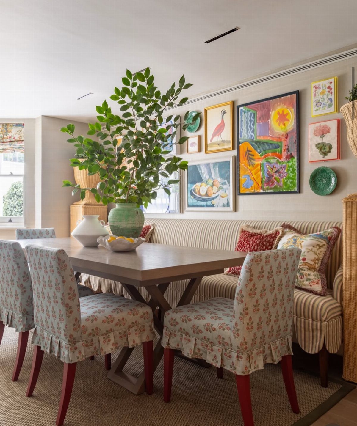 Dining area with a gallery wall of framed art and plates above a banquette.