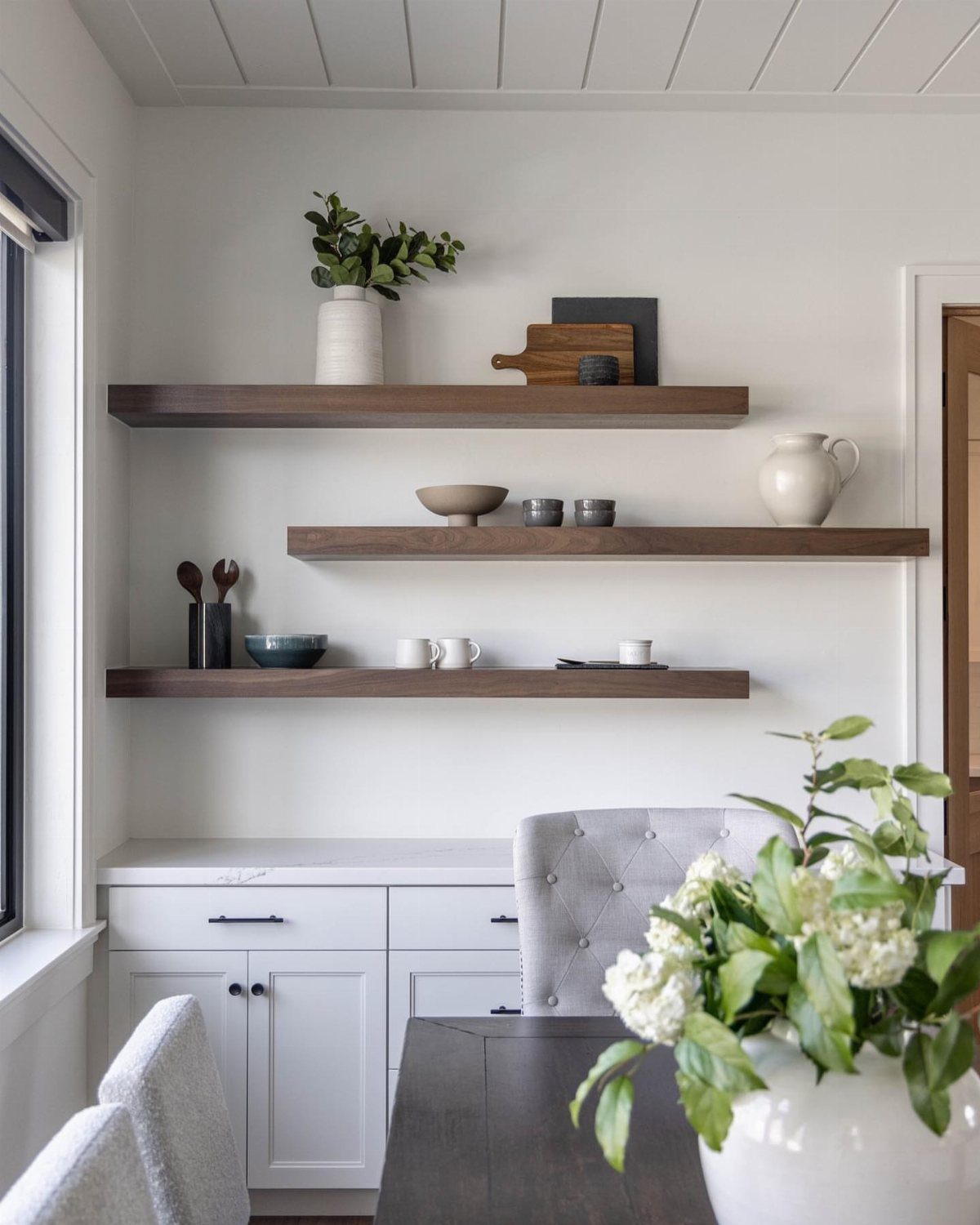 Dark wood floating shelves on a white wall holding decorative kitchenware and greenery.