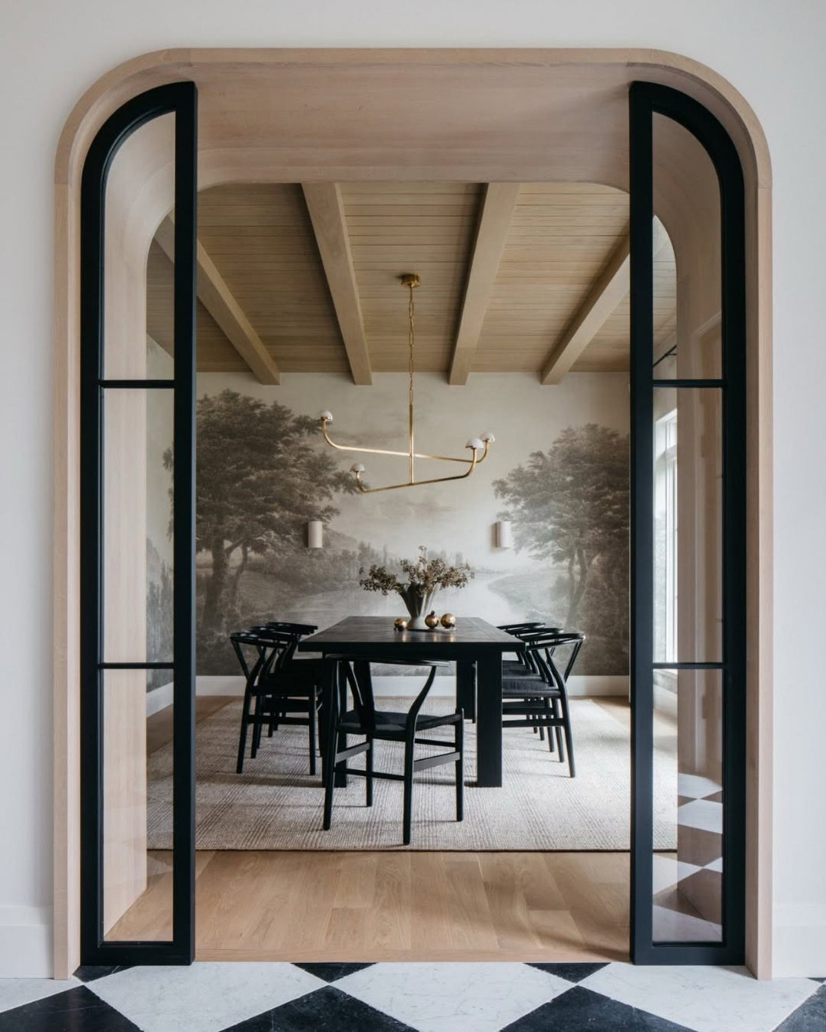 Dining room with a large landscape wall mural, black furniture, and arched entryway.