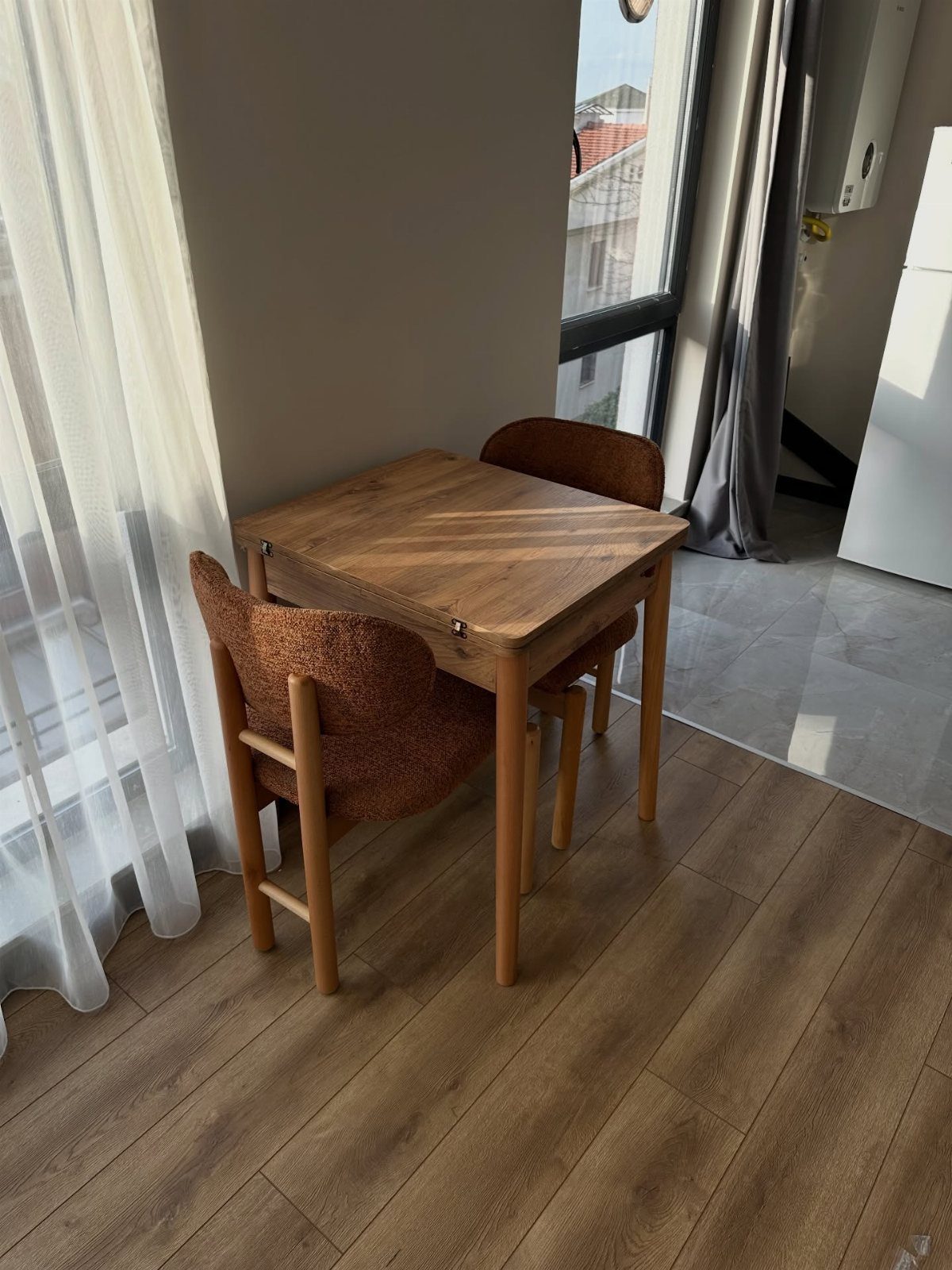 Wooden dining table and two brown chairs placed against a wall by a window.