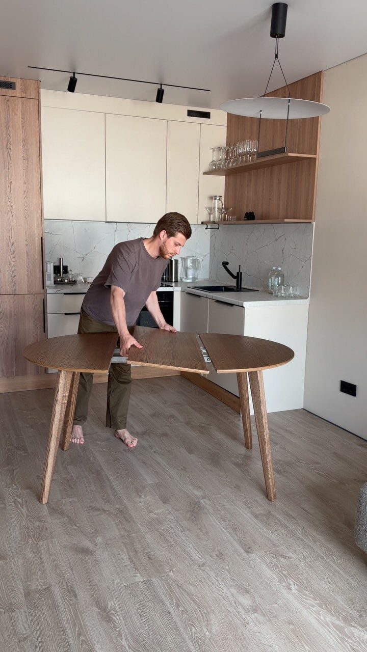 Man expanding a light brown wooden oval dining table in a modern kitchen