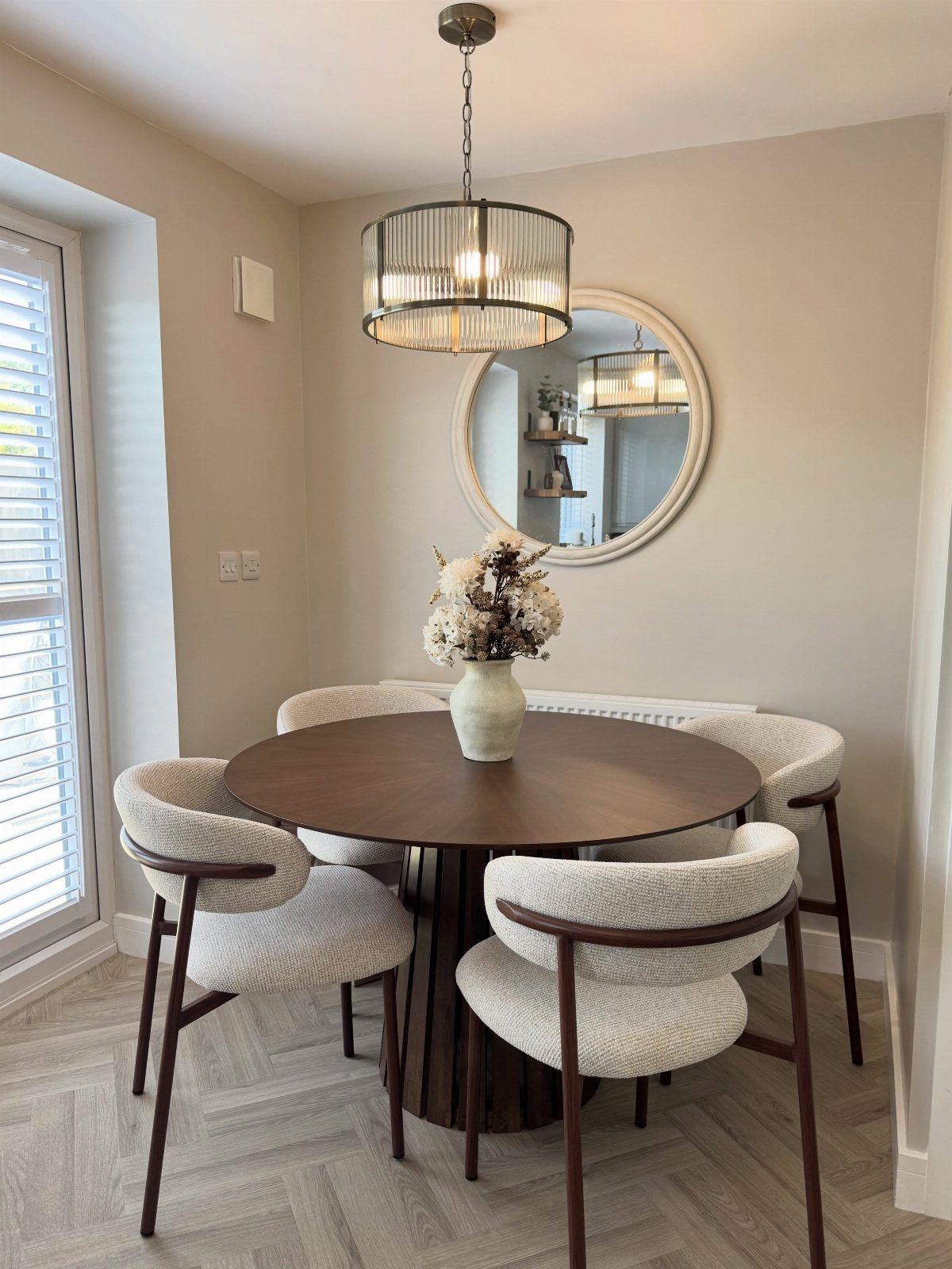 Round dark wood dining table with white chairs in a neutral modern room