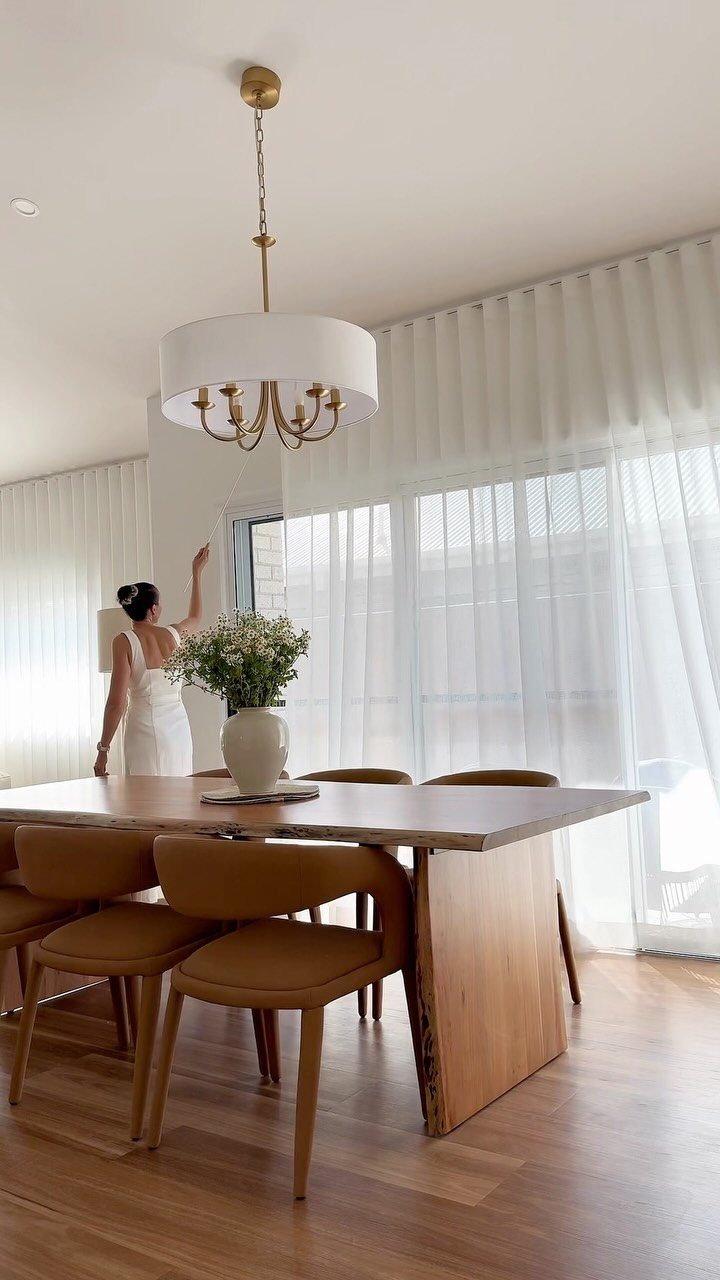 Dining room with a wooden table and white sheer curtains covering large windows.