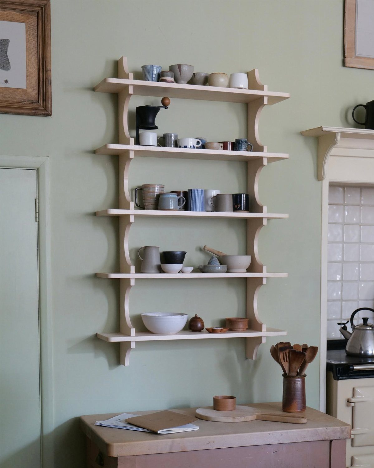Wooden wall-mounted shelves holding ceramic mugs and bowls against a pale green wall.