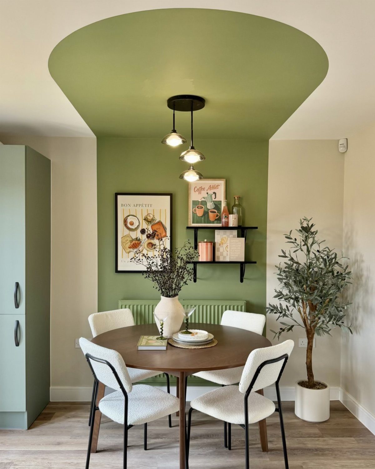 Sage green color-blocked wall and ceiling above a round wooden dining table