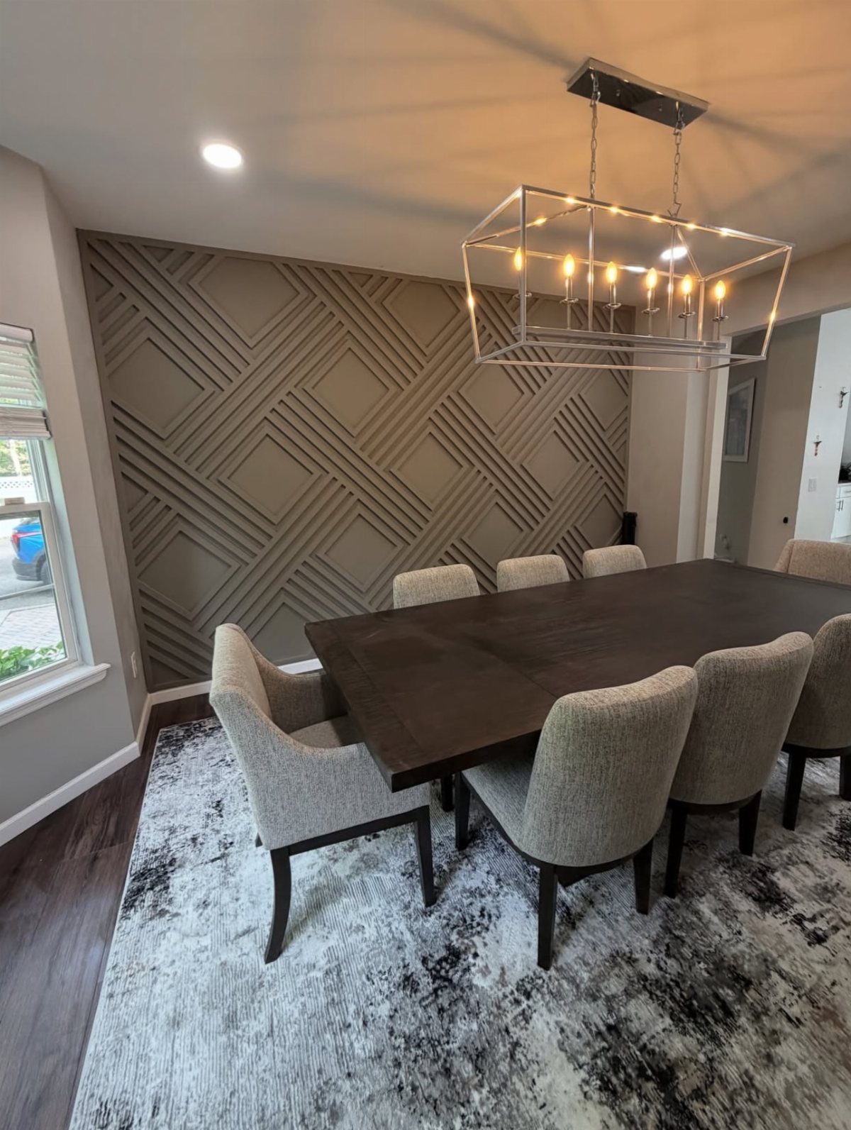 Dining room with a grey geometric paneled accent wall and dark wood table.