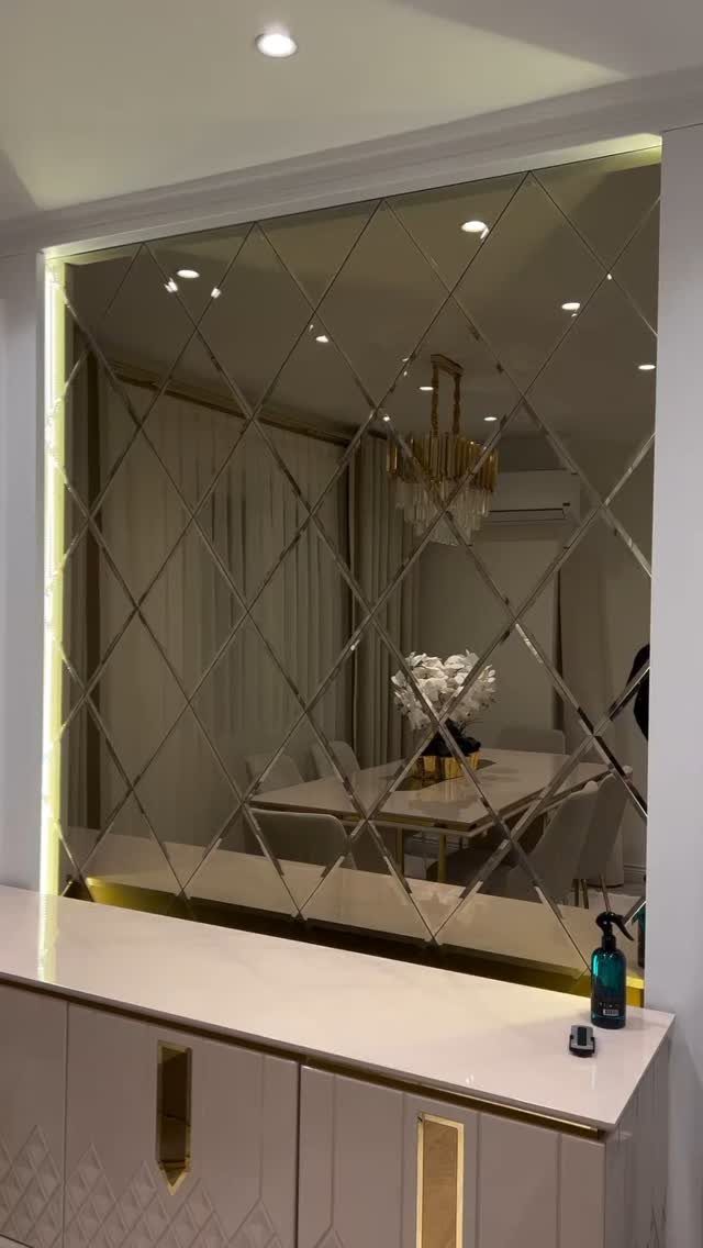 Diamond-patterned mirror accent wall reflecting a modern dining room with white furniture.