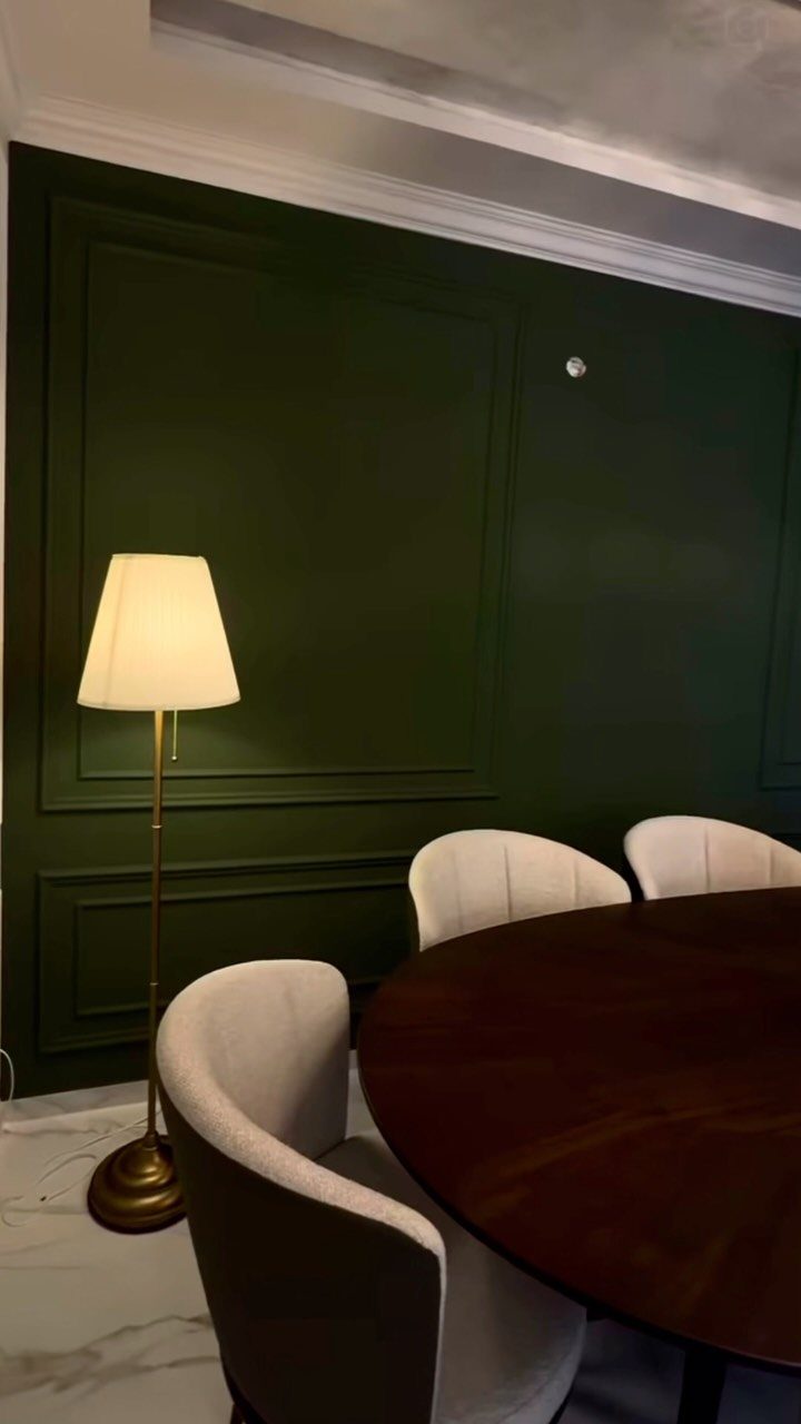 Dark green wall with wainscoting panels behind a round wooden dining table.