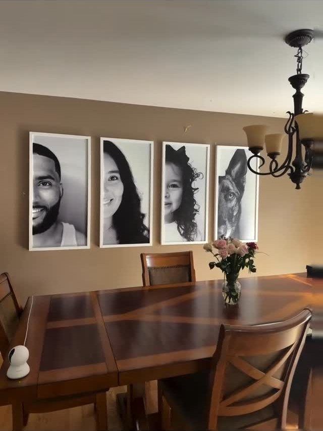 Four black and white portraits in white frames hanging in a line above a table.