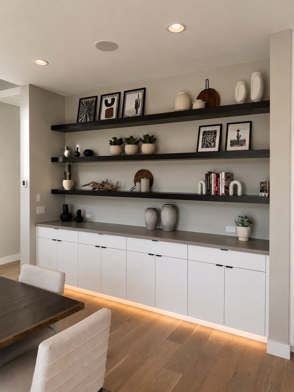 White lower cabinets and black floating shelves with decor in a modern dining area.