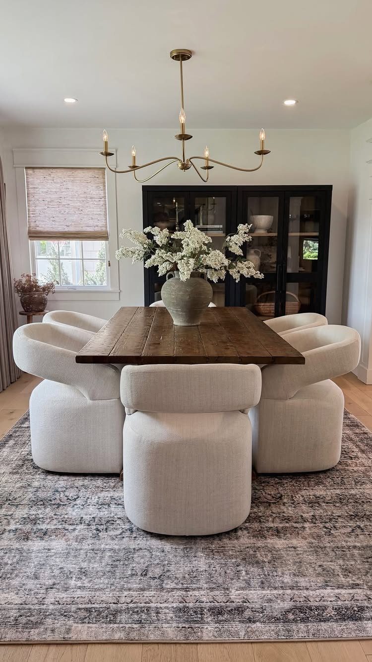 Wooden dining table with white curved chairs on a grey patterned area rug.