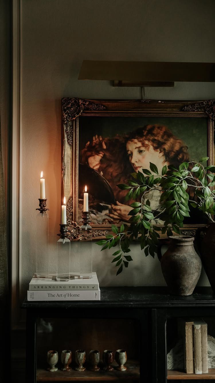 Classical portrait painting and lit candles on a dark wooden buffet table.