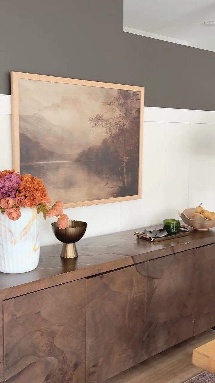 Dark wood buffet sideboard decorated with flowers, gold bowls, and a landscape painting.