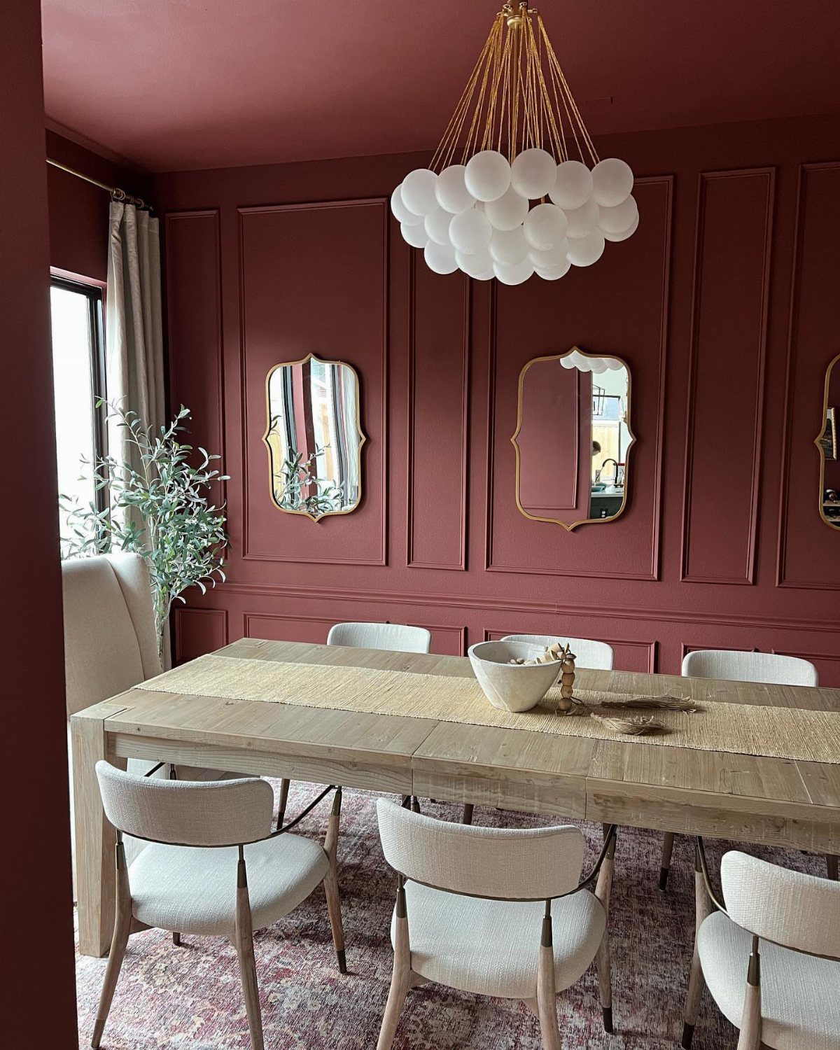 Dining room with red walls, decorative chair rail, and light wood table.