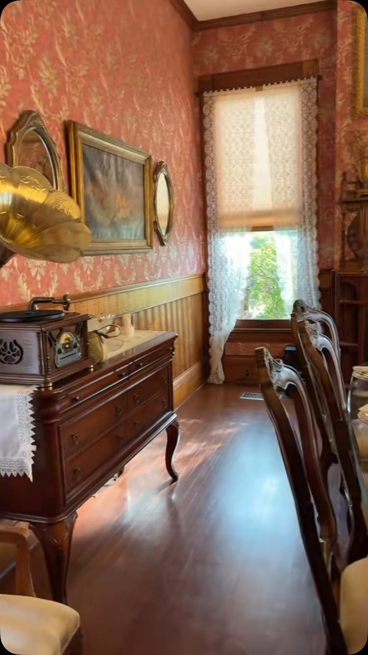 Vintage dining room featuring a wooden chair rail and red patterned wallpaper.