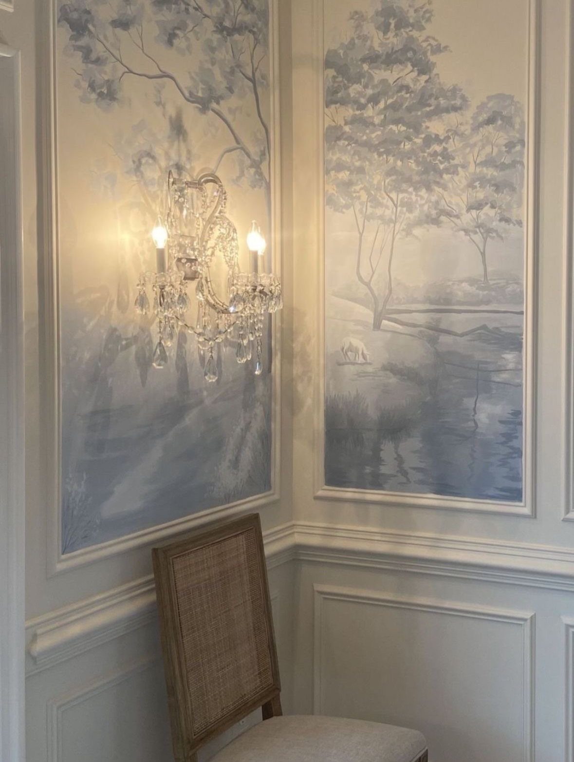 White chair rail separating blue landscape murals from white wainscoting in a dining room.