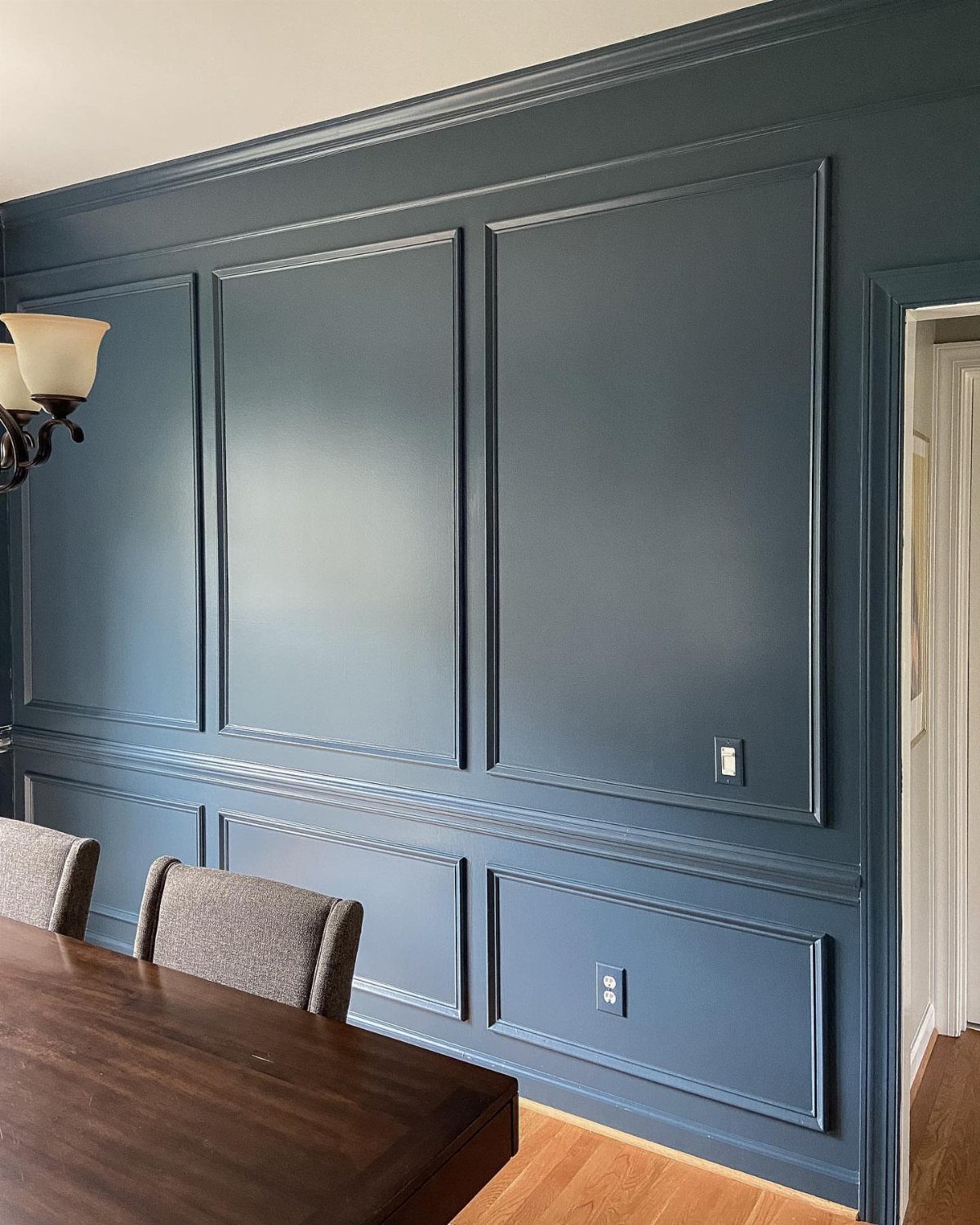 Deep navy blue dining room walls with elegant wainscoting and a dark wood table.
