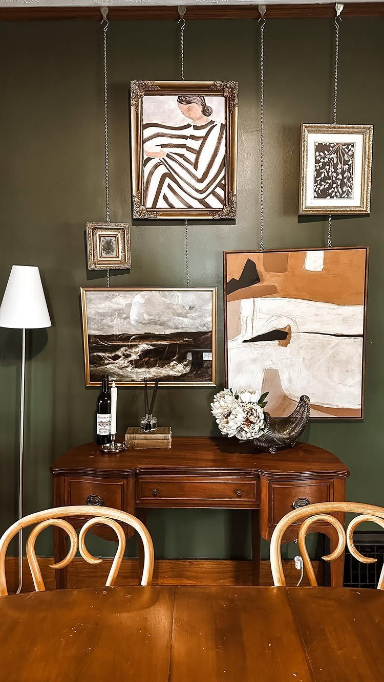 Olive green dining room walls with wooden furniture and hanging framed art pieces.