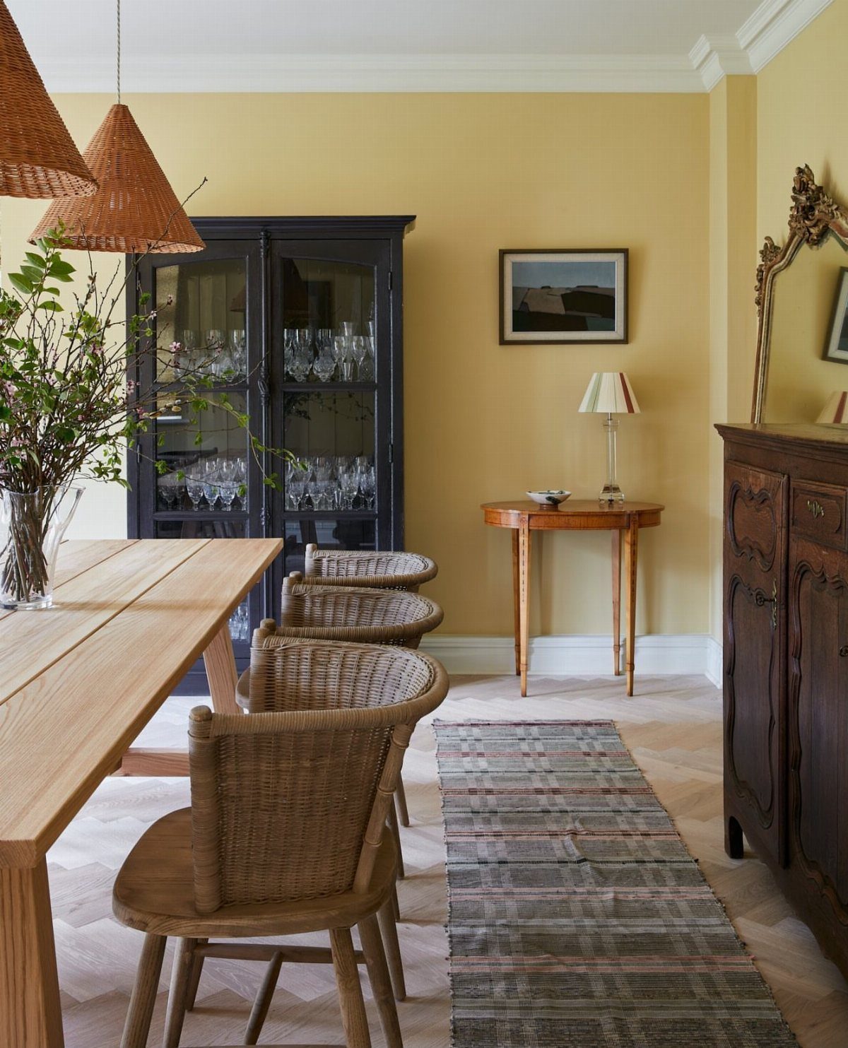 Dining room with pale yellow walls, light wood table, and woven chairs.