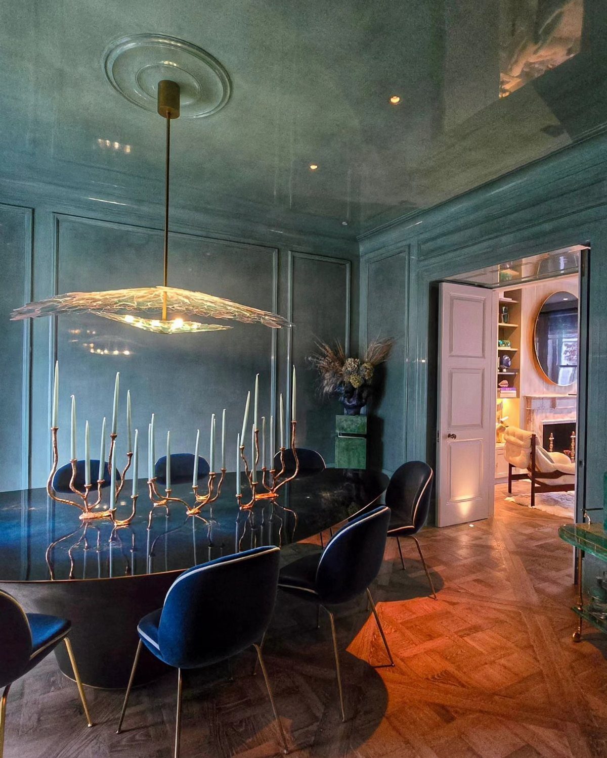 Teal-blue dining room with a black oval table and dark blue velvet chairs.