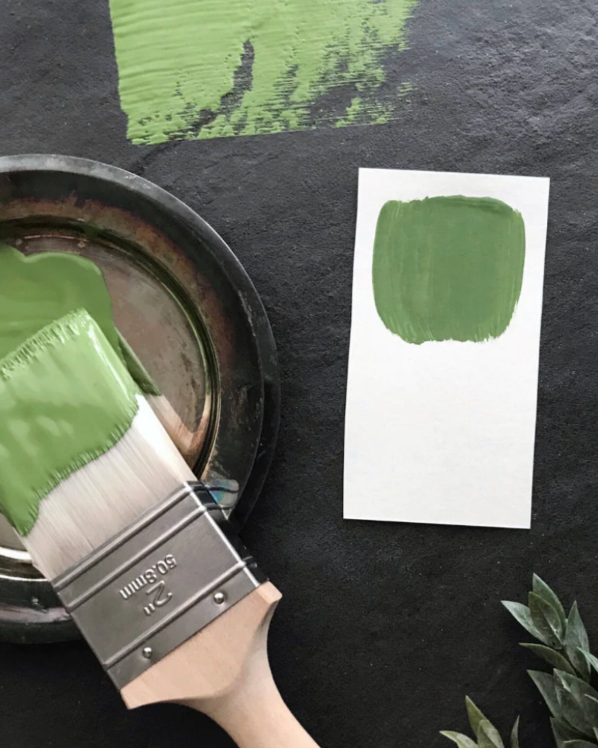 Paintbrush and green paint swatch on a dark surface for color testing.